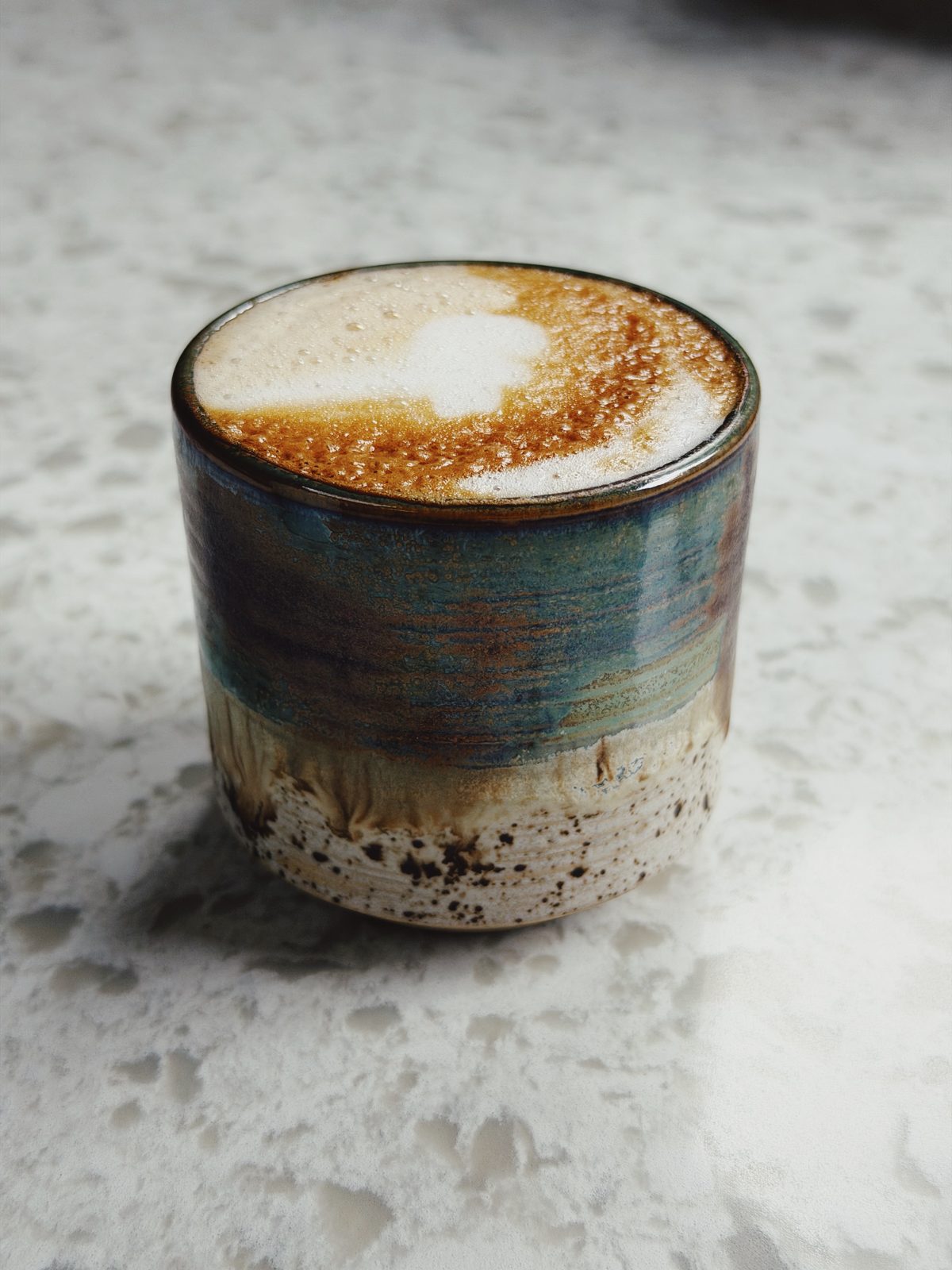 Cappuccino in een kopje met blauwgroen en gespikkeld glazuur